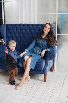 Portrait of gorgeous brunette young woman in casual denim dress embracing her lovely son in denim shirt on the bed. Family and motherhood concept.