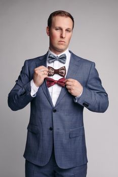 Selective focus of smiling man keeping bow ties in hand on isolated background. Young man wearing smart suit and white shirt looking at camera and posing in studio. Concept of official clothes.