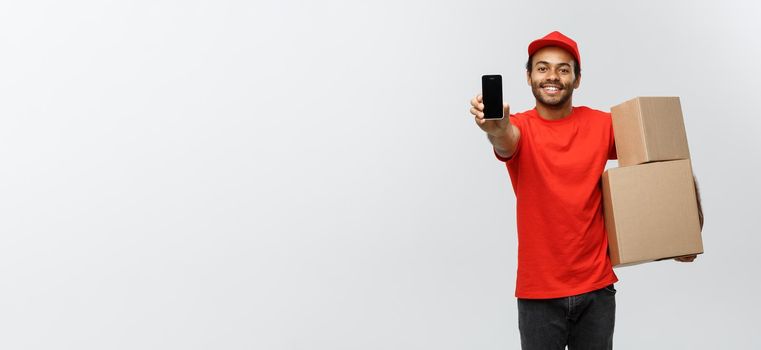 Delivery Concept - Portrait of Handsome African American delivery man or courier with box showing mobile phone on you to check the order. Isolated on Grey studio Background. Copy Space