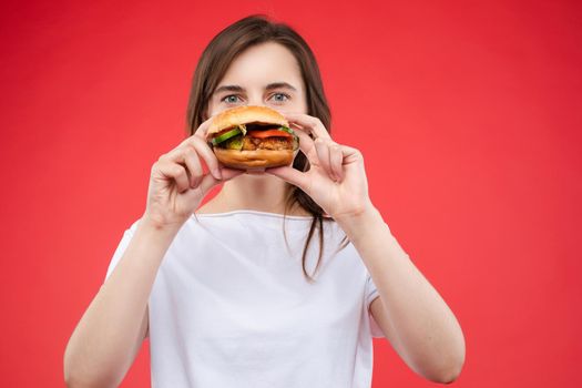 Medium close-up portrait of beautiful young fashion woman biting fresh appetizing sandwich. Portrait of smiling adorable female posing enjoying eating fast food in cafe