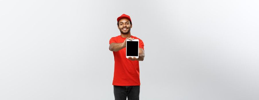 Delivery Concept - Portrait of Handsome African American delivery man or courier showing tablet on you to check the order. Isolated on Grey studio Background. Copy Space