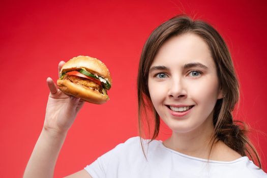 Medium close-up portrait of beautiful young fashion woman biting fresh appetizing sandwich. Portrait of smiling adorable female posing enjoying eating fast food in cafe