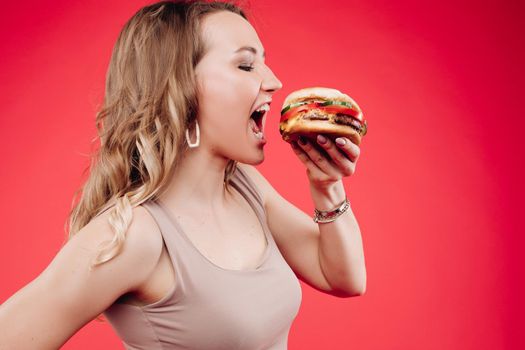 Medium close-up portrait of beautiful young fashion woman biting fresh appetizing sandwich. Portrait of smiling adorable female posing enjoying eating fast food in cafe