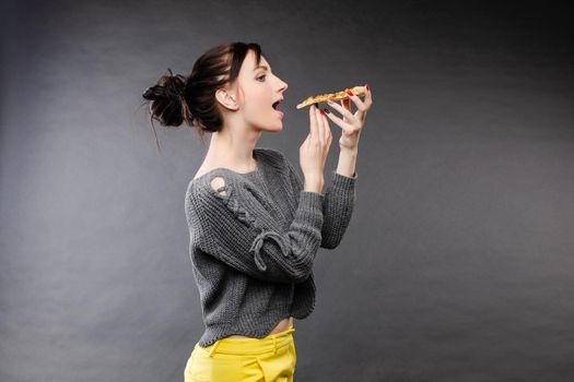 Close up of hungry girl with opened mouth, holding and eating pizza. Pretty woman pizza eating tasty pizza with tomato and meal. Concept of fast food.