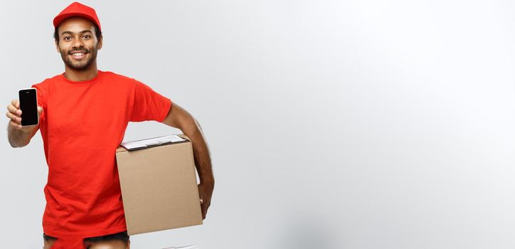 Delivery Concept - Portrait of Handsome African American delivery man or courier with box showing mobile phone on you to check the order. Isolated on Grey studio Background. Copy Space