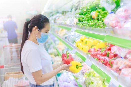 Asian woman wear face mask push shopping cart in supermarket. female looking grocery to buy something During coronavirus crisis or covid19 outbreak. Women wearing protective face mask new normal concept