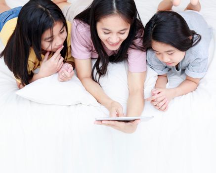 Top view Happy Asian family enjoy and relax on bed in bedroom. mother and daughters enjoy using tablet together on bed.  Family concept.