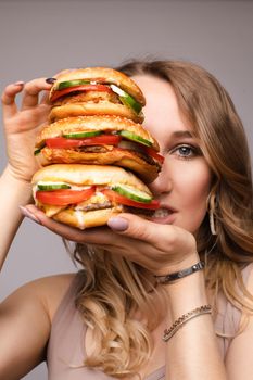 Studio portrait of young brunette woman in white t-shirt holding enormous burgers on her hand looking shocked or surprised at camera.
