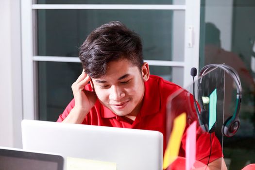 Smiling young man using laptop at home in living room. Asian young man working at office with laptop. Man reoax after work at office. Business concept.
