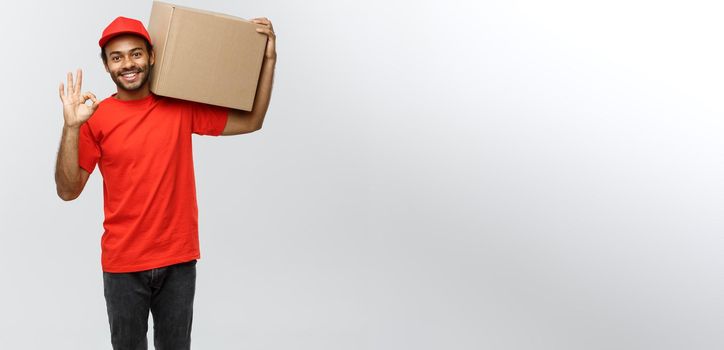 Delivery Concept - Portrait of Happy African American delivery man holding a box package and showing ok sign. Isolated on Grey studio Background. Copy Space