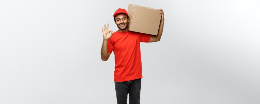 Delivery Concept - Portrait of Happy African American delivery man holding a box package and showing ok sign. Isolated on Grey studio Background. Copy Space