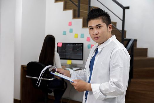 Asian small business start up working at Private Home Office.. Businessman holding and analysis document paper chart  with blur partner sitting and working background