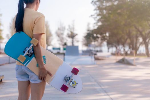 Close up on young women hand hold skateboard, surf skate on public skate ramp park background. Free relax skateboard surf skate trendy concept. Fashion portrait of female hands holding surf skateboard