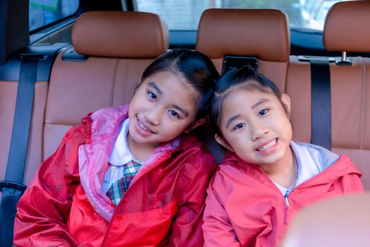 Two happy students smiling while enjoying road trip in car. Sisters smiling and looking camera inside car in morning. Asian cildrens sitting in car on the way go to school. Family in car