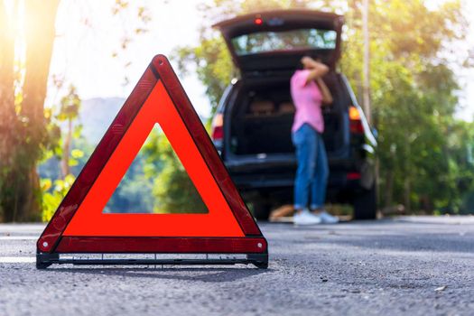 Close up red emergency stop sign standing on road. Worried and angry woman walking near his broken car talking on phone with insurance agent. Close up triangle on side road