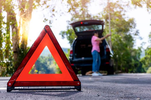 Close up red emergency stop sign standing on road. Worried and angry woman walking near his broken car talking on phone with insurance agent. Close up triangle on side road