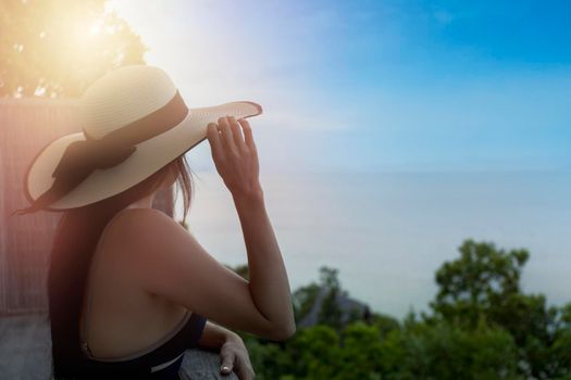Rear view of young woman tourist standing and relax view from hotel terrace to the sea and the horizon. Beautiful woman admires the view after the long-awaited arrival on vacation. Holiday summer concept