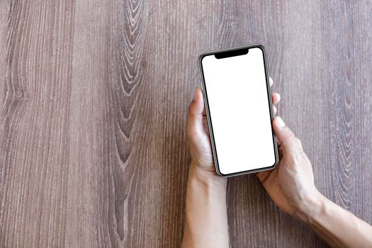 Top view female hands holding smart phone with blank white screen. Women hands workspace, close-up hand holding smartphone blank screen for text and content on wood table background.
