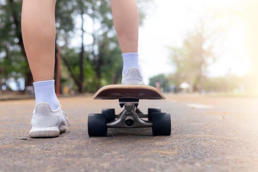 Close up rear view Asian women leg on surf skate or skate board in outdoor Park. Closeup leg wear white sneakers put on surfskate at public park. Extreme sport and relax concept