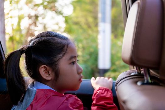 Asian Happy student smiling with camera while enjoying road trip in car. Daughter smiling and looking camera inside car in morning. Asian children's sitting in car on the way go to school. Family in car