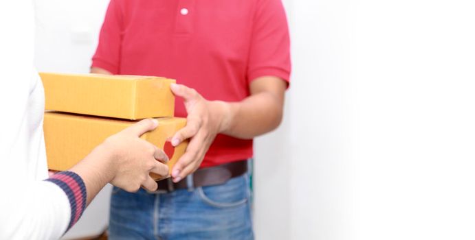 Delivery man delivering package to homeowner. Woman hand accepting a delivery of boxes from deliveryman. Delivery man wear red uniform sent box package to women hand. Delivery concept.