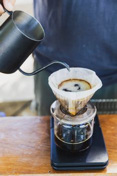 Barista spills hot water prepare filtered coffee from stainless steel teapot to drip paper maker on black simple weights. Everything thick wooden table cafe shop. Steam. Process vintage style