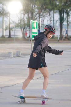 Asian women on skates board outdoors on beautiful summer day. Happy young women play surfskate at park on morning time. Sport activity lifestyle concept