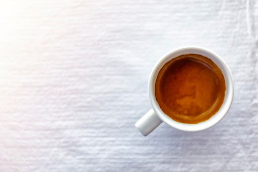 Top view close up of hot espresso coffee in a white ceramic cup on a white tablecloth background on morning
