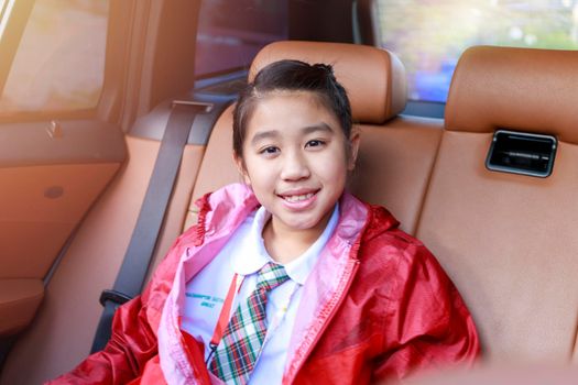 Asian Happy student smiling with camera while enjoying road trip in car. Daughter smiling and looking camera inside car in morning. Asian cildrens sitting in car on the way go to school. Family in car