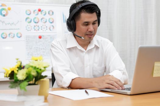 Asian businessman talking with team via video conference writing note on paper. business people using laptop and headset for online meeting. Man using headphone speak with customers. work from home concept.