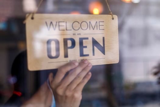 Hand of asian owner retail ,coffee shop woman turning sign board to open. Protection to pandemic of coronavirus. Open store,restaurant or pub due to lockdown quarantine of covid-19.
