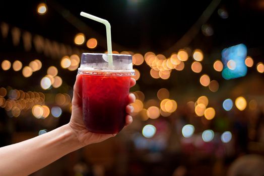 Hand of asian women holding the famous thai Iced back tea at night market with bokeh light of night market background