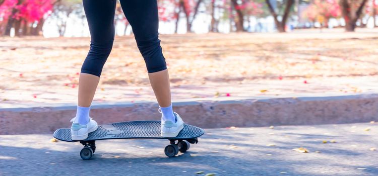 Close-up and motion movement Asian women surf skate or skateboard outdoors on beautiful morning. Happy young women play surf skate at park on morning time. Close up Asian women leg wear sneaker paly surf skate on public park. Sport concept