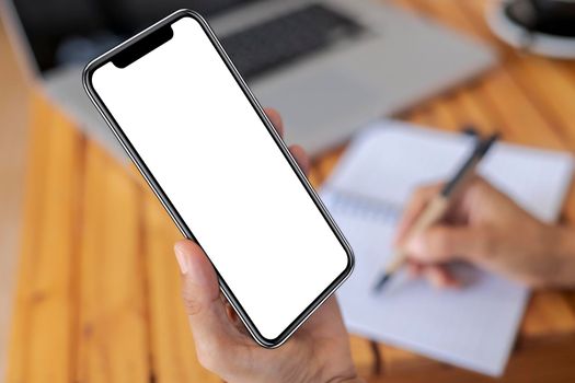 Top view female hands holding smart phone with blank white screen. Women hands workspace, close-up hand holding smartphone blank screen for text and content on wood table background.