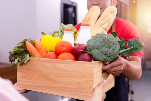Asian deliver man in red uniform handling wooden crate box of food, fruit, vegetable give to female costumer. Postman and express grocery delivery service