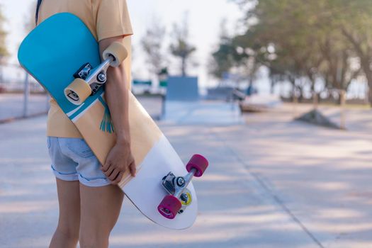 Close up on young women hand hold skateboard, surf skate on public skate ramp park background. Free relax skateboard surf skate trendy concept. Fashion portrait of female hands holding surf skateboard