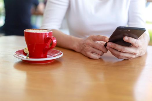 Close up hands of beautiful young woman holding mobile, smart phone sitting in cafe. Soft focus hands of women holding and use cell phone in coffee shop. Tectechnology and lifestyle concept.