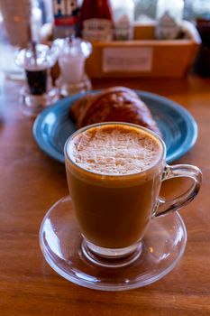 Close up hot cappuccino, latte, caramel macchiato on table with blur coffee shop background. Hot cappuccino coffee on wood table with blur croissant background. breakfast at coffee shop. softfocus select coffee