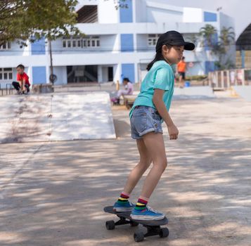 Little asian girl play surf skate board at park skate ramp outdoors on morning. Happy girl play surfskate board at park . Sport activity lifestyle concept