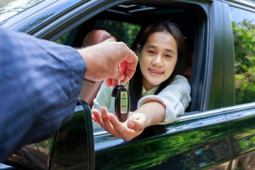 Close up of dealer giving key to new owner car. New car. Auto dealer giving woman automobile key for test drive on country road. Soft focus  smiling women try to test drive a car on road with dealer.