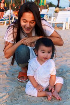 Happy family Mother and her little daughter play at the beach together. Happy little girl relax and sit on the beach with her mother. smiling mother play with her daughter