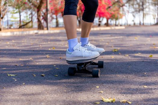 Close-up and motion movement Asian women surf skate or skateboard outdoors on beautiful morning. Happy young women play surf skate at park on morning time. Close up Asian women leg wear sneaker paly surf skate on public park. Sport concept