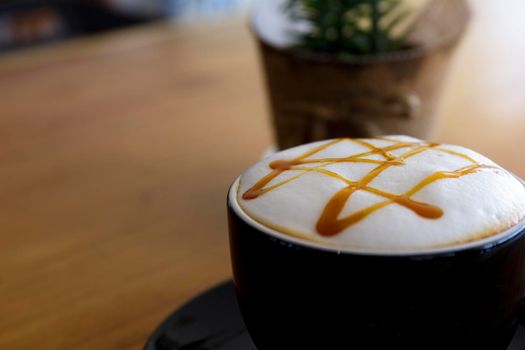 Close up hot cappuccino, latte, caramel macchiato on table with blur coffee shop background. Process with warm vintage tone style.