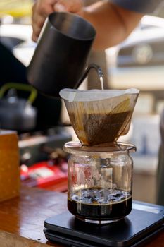 Barista spills hot water prepare filter coffee from stainless steel teapot to drip paper maker on black simple weights. Everything thick wooden table cafe shop. Steam. Process vintage style
