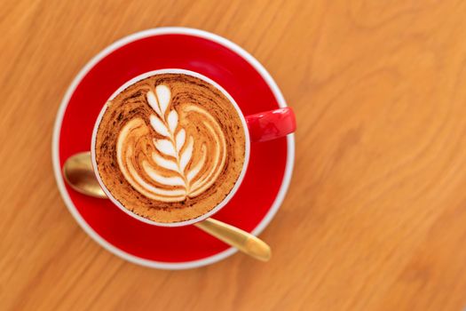 Soft focus Top view close up of hot espresso, latte coffee in a red ceramic cup on blur wood table background.