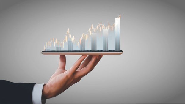 Hand of businessman holding tablet analysis stock market graph growth and increase of chart positive indicators. Hand holding tablet show stock chart on light gray background