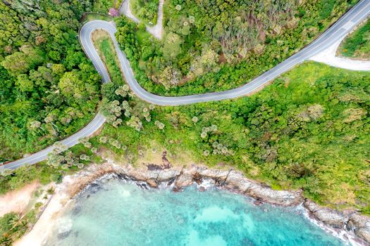 Aerial drone top down view of waves breaking in the sand with road and forest. High angle view of tropical sea with Seafront road. Phuket Thailand curves of coastal road. Phuket is famous tourist destination. Top view traffic road around the beach