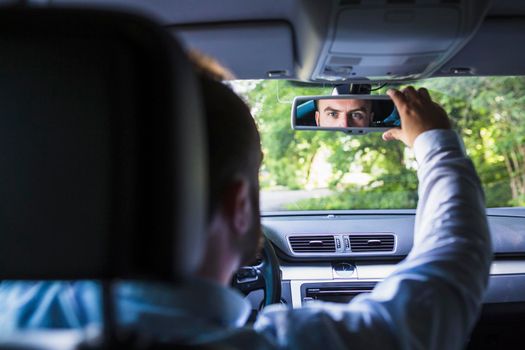 man sitting inside car adjusting rear view mirror