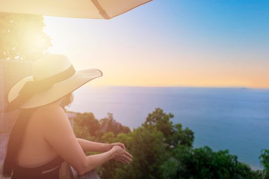 Rear view of young woman tourist standing and relax view from hotel terrace to the sea and the horizon. Beautiful woman admires the view after the long-awaited arrival on vacation. Holiday summer concept