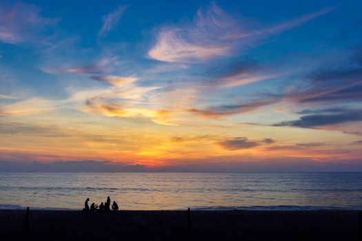 Silhouettes of group of people during the sunset in Seaside beach. Beautiful sunset over the sea with silhouettes happy group of people relax. Holiday and summer concept